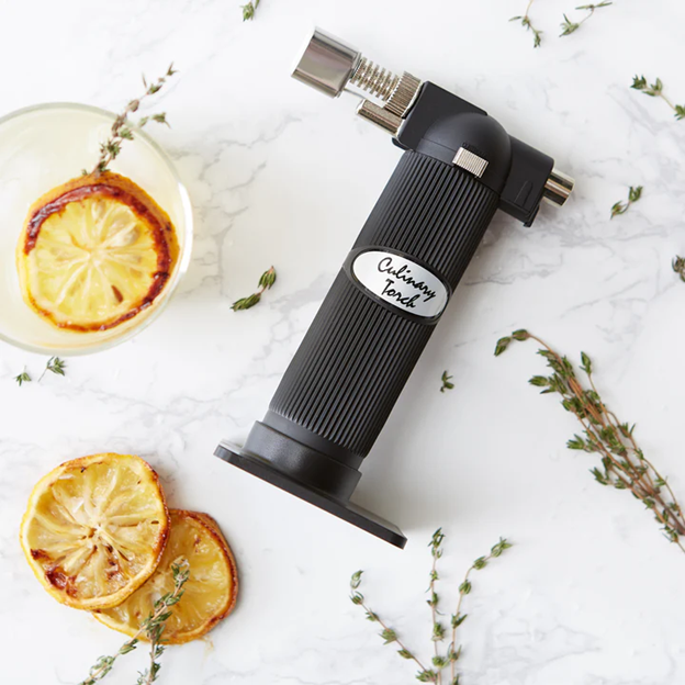 blow torch for cooking next to broiled fruit and herbs for garnishing