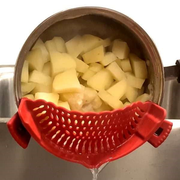 red silicone clip on strainer on pot draining water from boiled potatoes