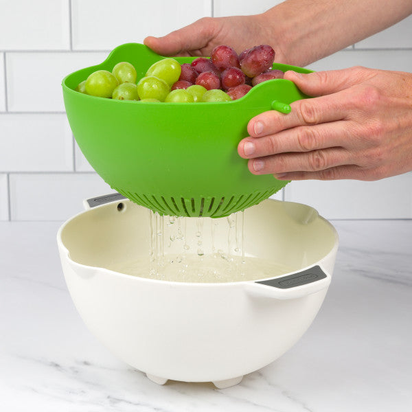 green colander with grapes straining into white bowl