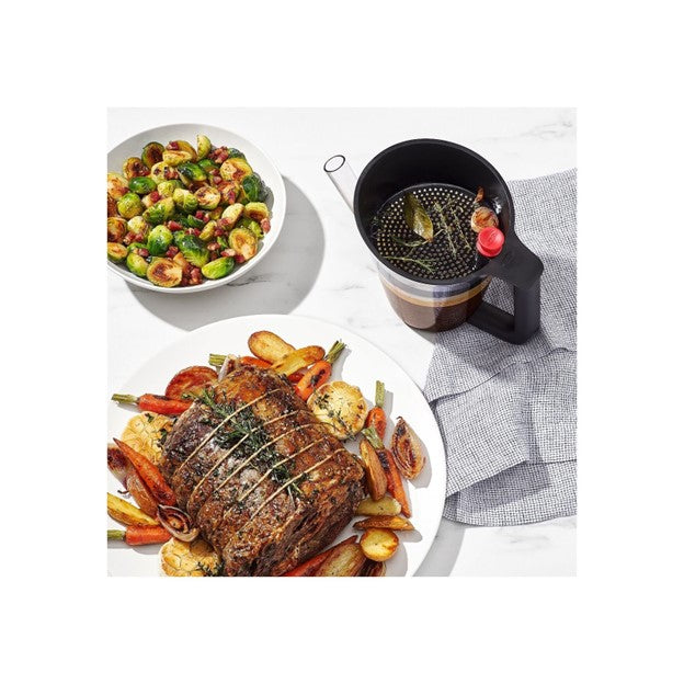 top view of fat separator on kitchen table next to plate of roasted meat and vegetables and bowl of roasted brussel sprouts