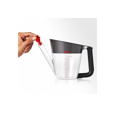 side view of empty oxo good grips fat separator for gravy with hand placing stopper in spout