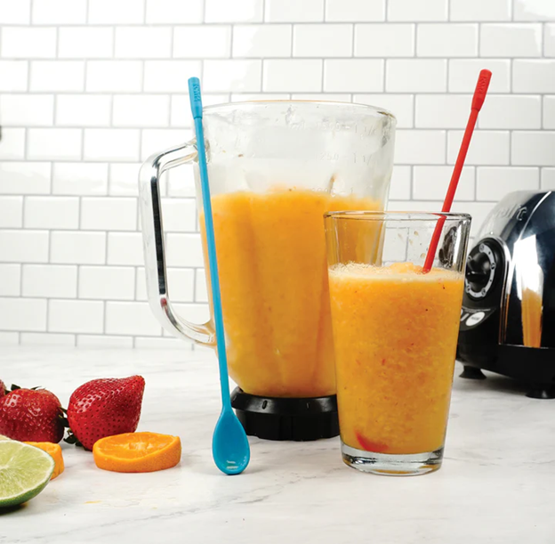 two long handle silicone spoons in a glass and next to a blender with smoothie, and fresh fruit on kitchen counter