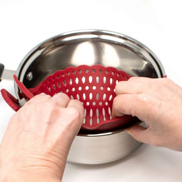 red silicone pasta strainer being placed into silver stainless pot