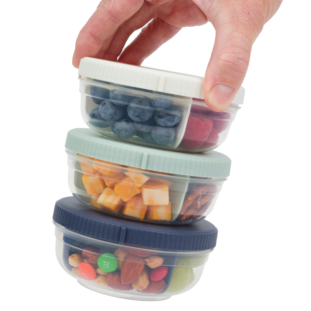 three plastic stackable food storage containers for snacks with snacks inside, stacked on top of each other, in navy, mint, and white colors