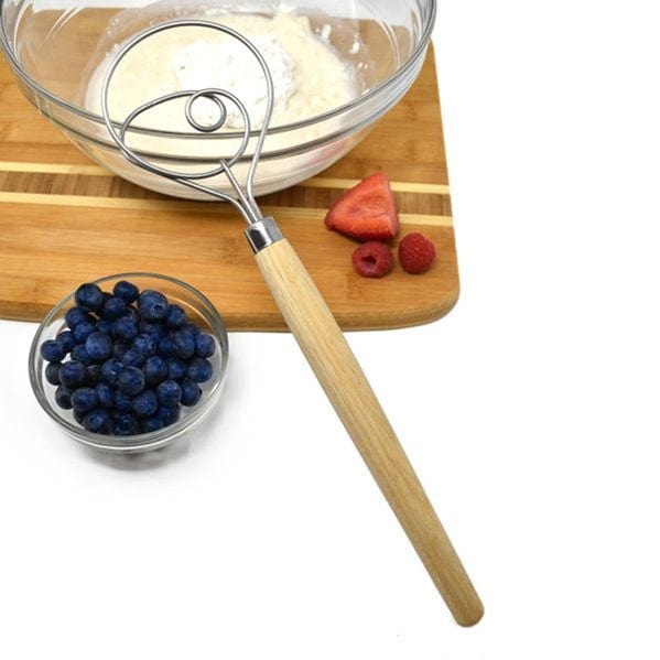 Norpro 12'' Danish Dough Whisk sitting on top of bread board with glass cup of blueberries next to mixing bowl with sourdough muffin batter and strawberries and raspberries on top of board